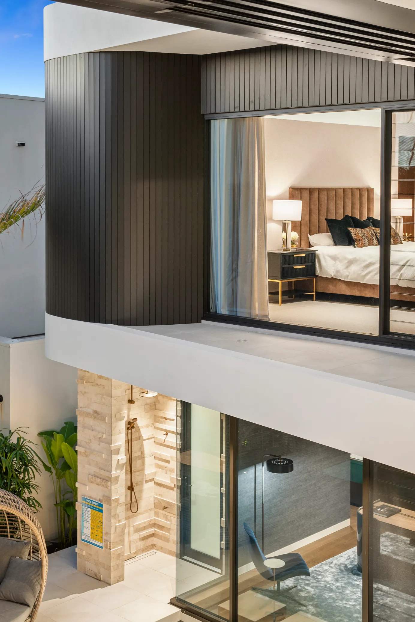 Multi-level modern architectural home at Knightsbridge Parade featuring a prominent textured stone outdoor shower, curved dark exterior cladding, and large bedroom windows.